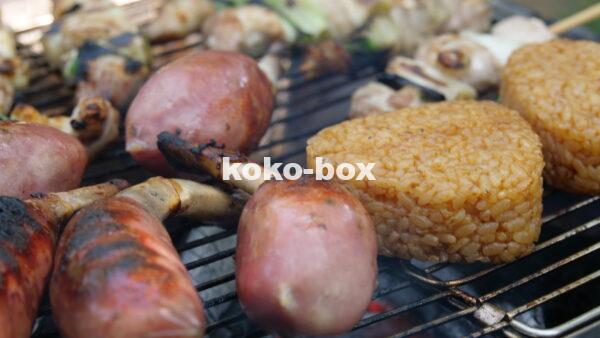 キャンプ場でバーベキュー。骨付き肉と焼きおにぎり、焼き鳥を炭火で焼いている写真