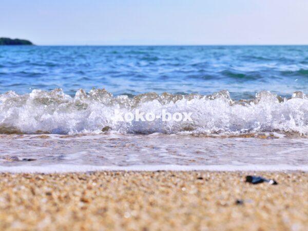 海の綺麗な青に白い波がはじける波打ち際と砂浜の写真
