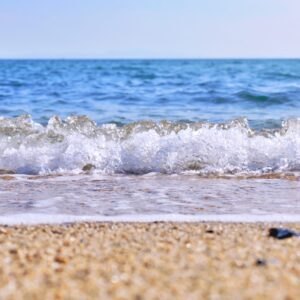海の綺麗な青に白い波がはじける波打ち際と砂浜の写真