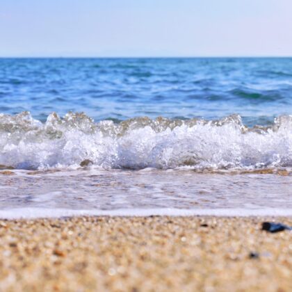 海の綺麗な青に白い波がはじける波打ち際と砂浜の写真