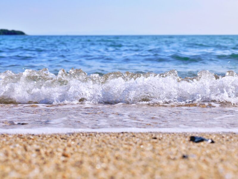 海の綺麗な青に白い波がはじける波打ち際と砂浜の写真