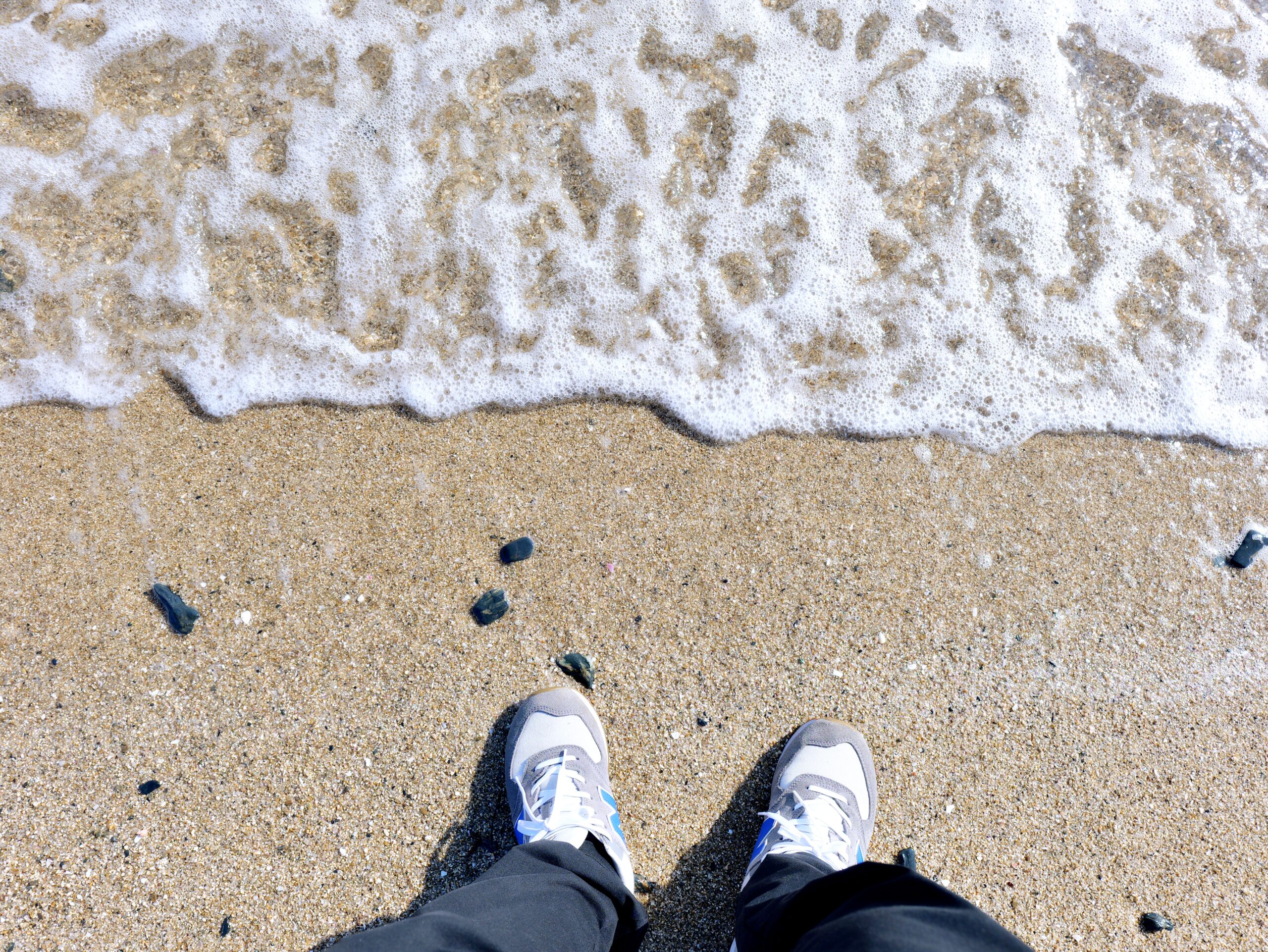 波打ち際に立つ人の足が写った波の写真