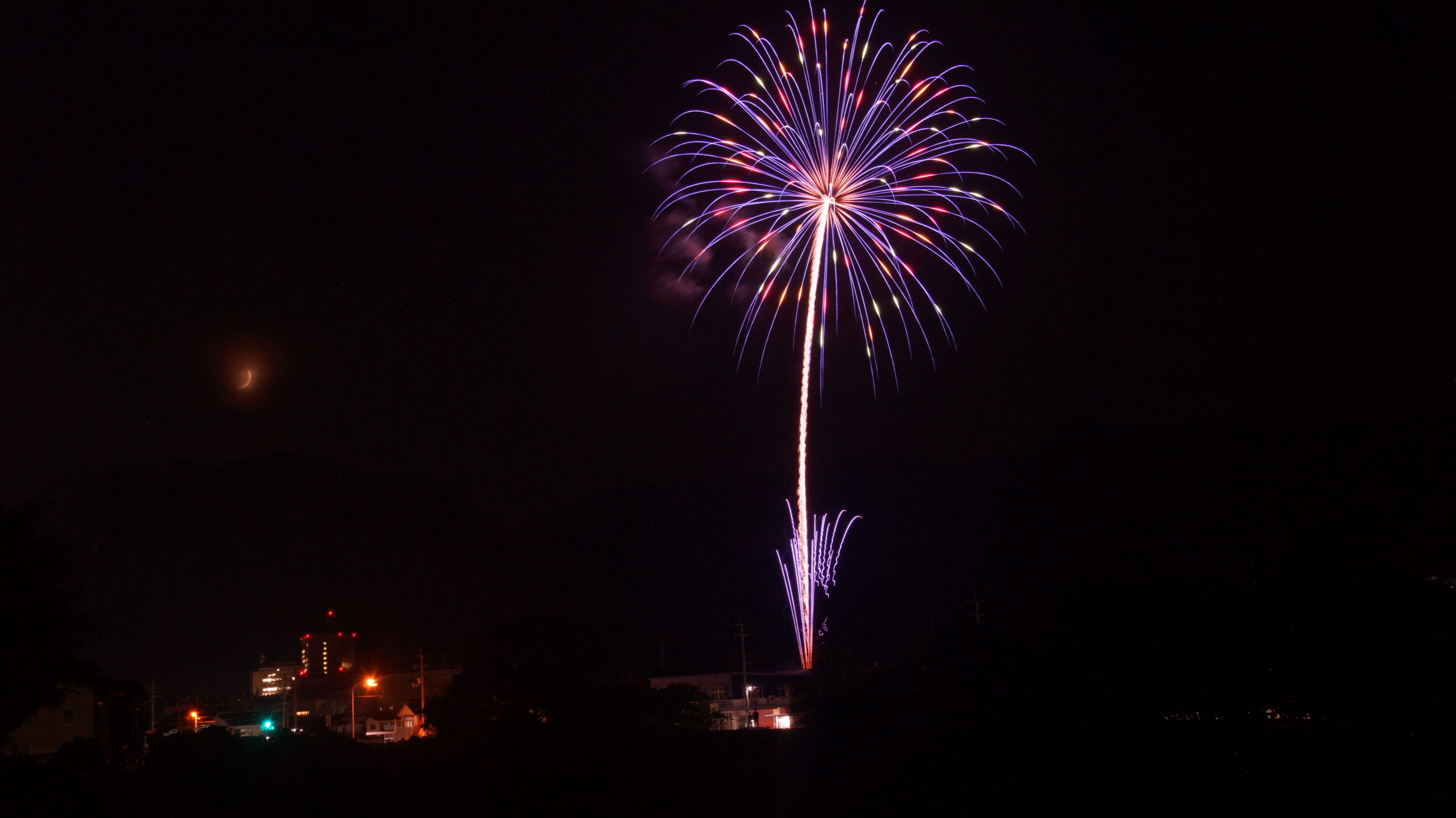 打ちあがった綺麗な紫色の花火と半月のコラボの写真