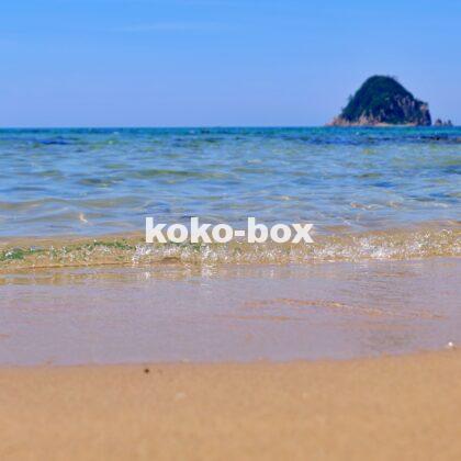 青い空と透き通るような海と白い砂浜と島が写った海岸の縦写真