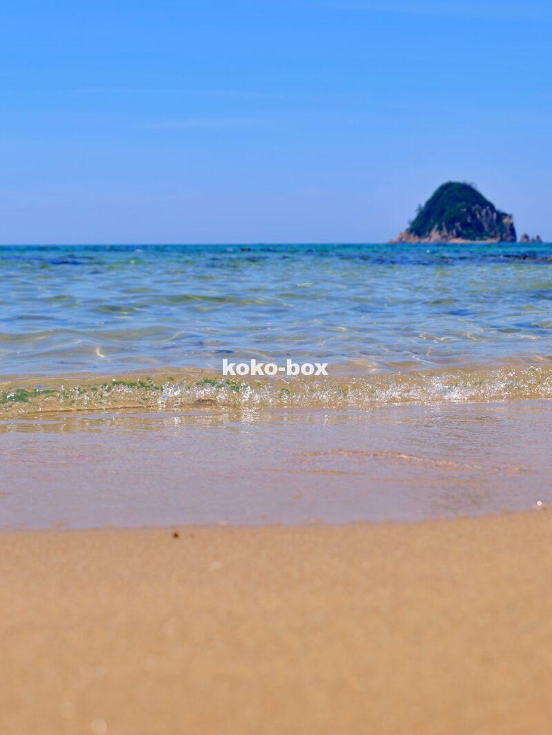 青い空と透き通るような海と白い砂浜と島が写った海岸の縦写真