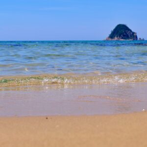 青い空と透き通るような海と白い砂浜と島が写った海岸の縦写真
