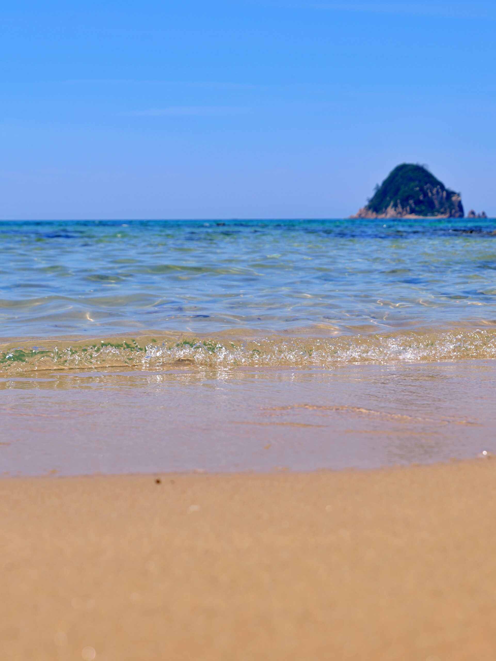 青い空と透き通るような海と白い砂浜と島が写った海岸の縦写真