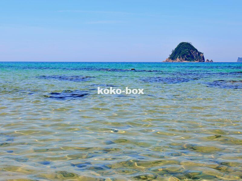 青い空と透き通るような海と島が写った海岸の写真