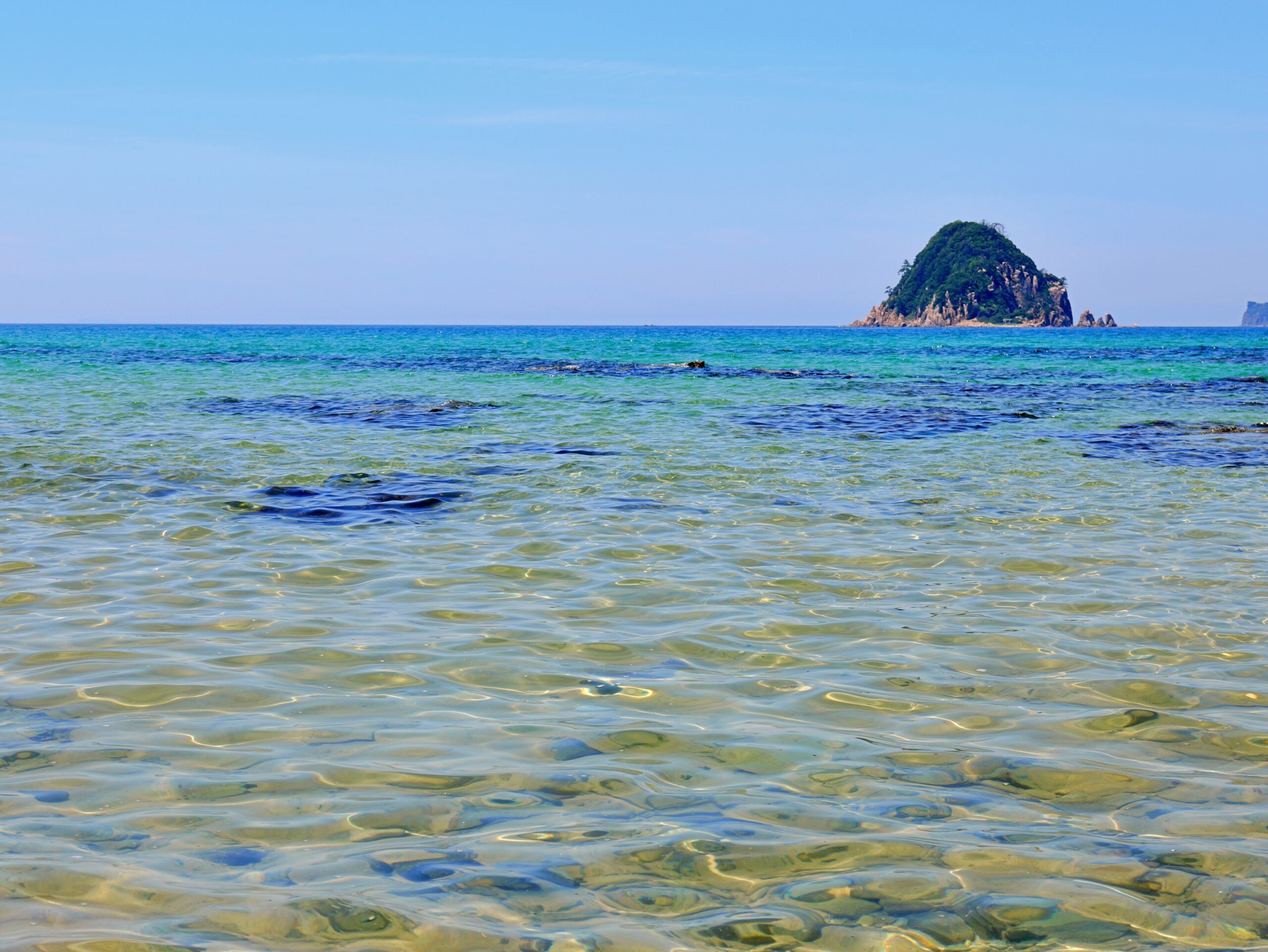 青い空と透き通るような海と島が写った海岸の写真