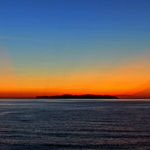 水平線と島から伸びる赤とオレンジの射線が綺麗なグラデーションの夕焼けの写真