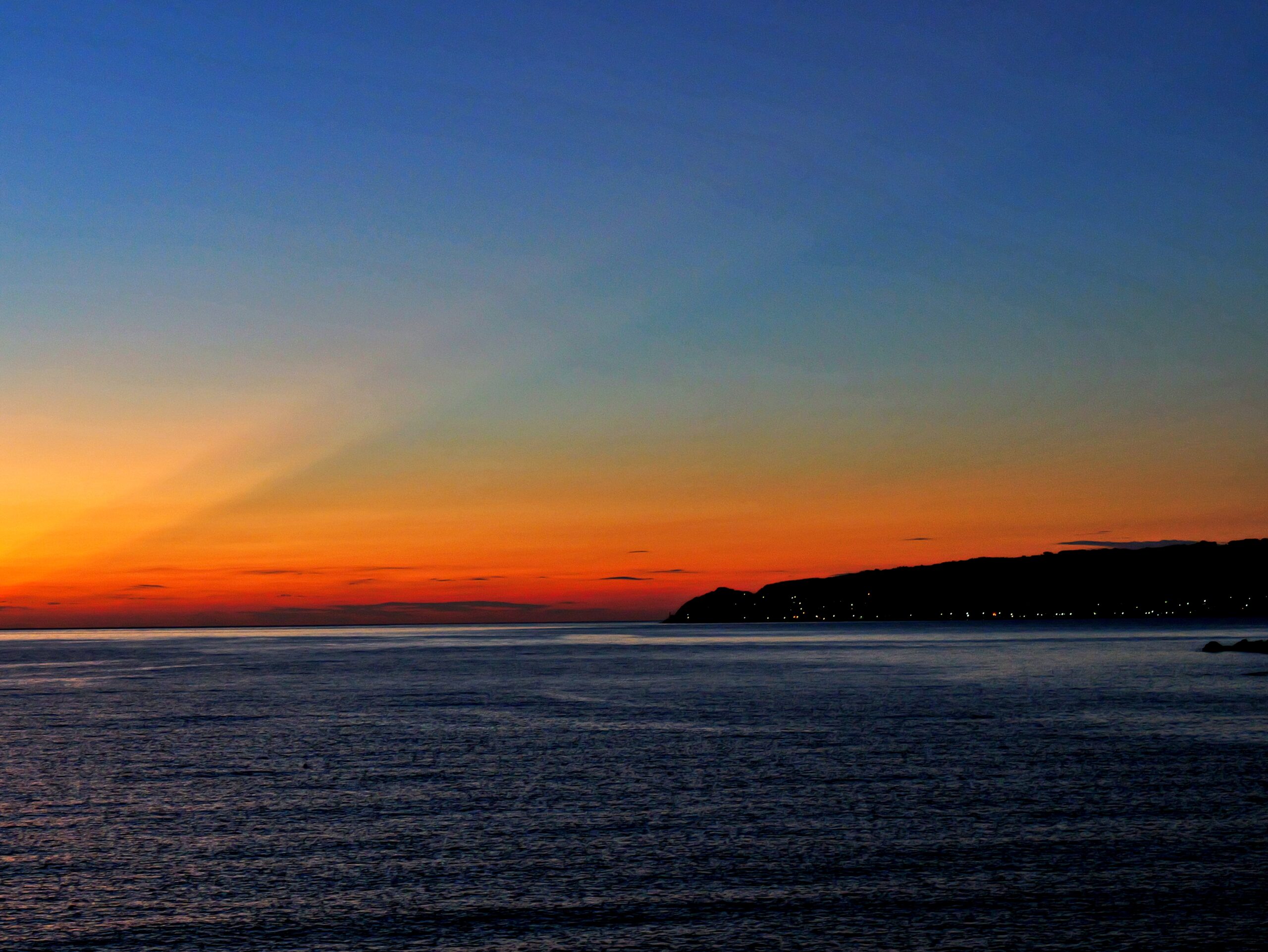 水平線と島から伸びる赤とオレンジの幻想的な射線を強調した綺麗なグラデーションの夕焼けの写真