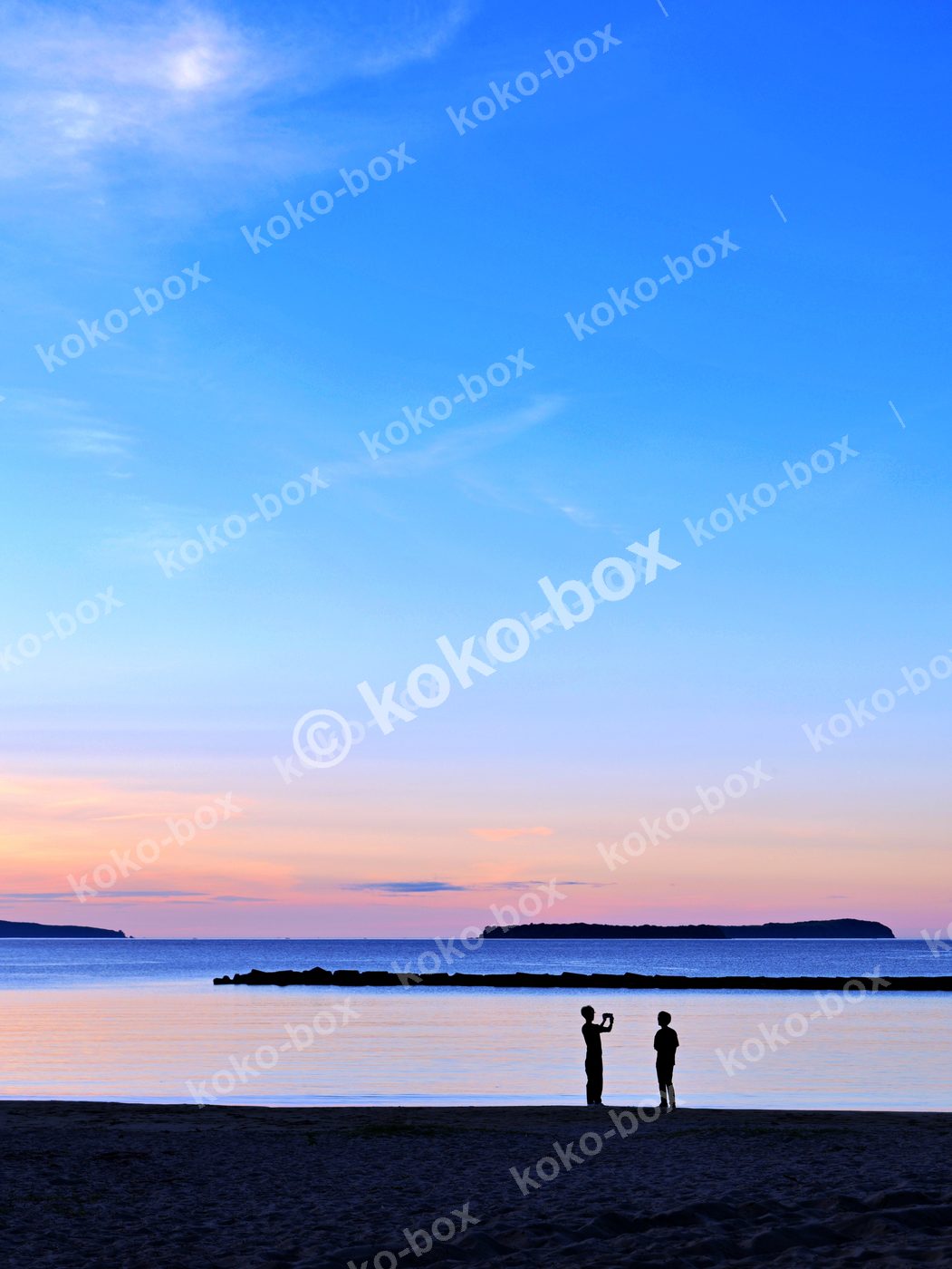 夕暮れの海辺と二人のシルエット 縦位置写真素材