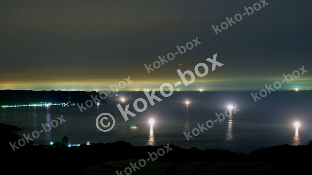 赤い月と漁火、街の光が輝く幻想的な夜景写真素材