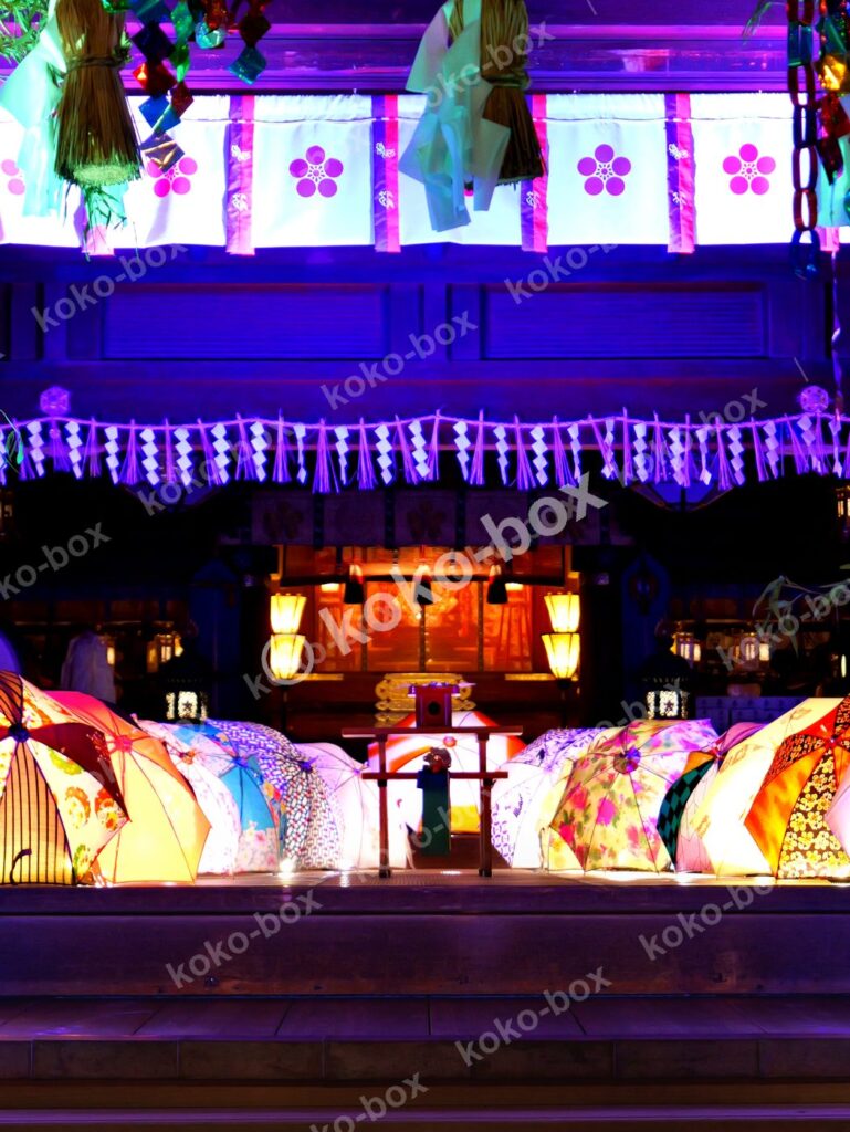 夜の神社に並べられたカラフルな和傘と提灯のイルミネーションの縦位置写真