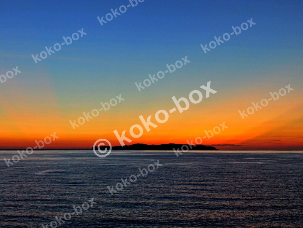水平線と島、赤オレンジの射線が美しい夕焼けグラデーション 写真素材