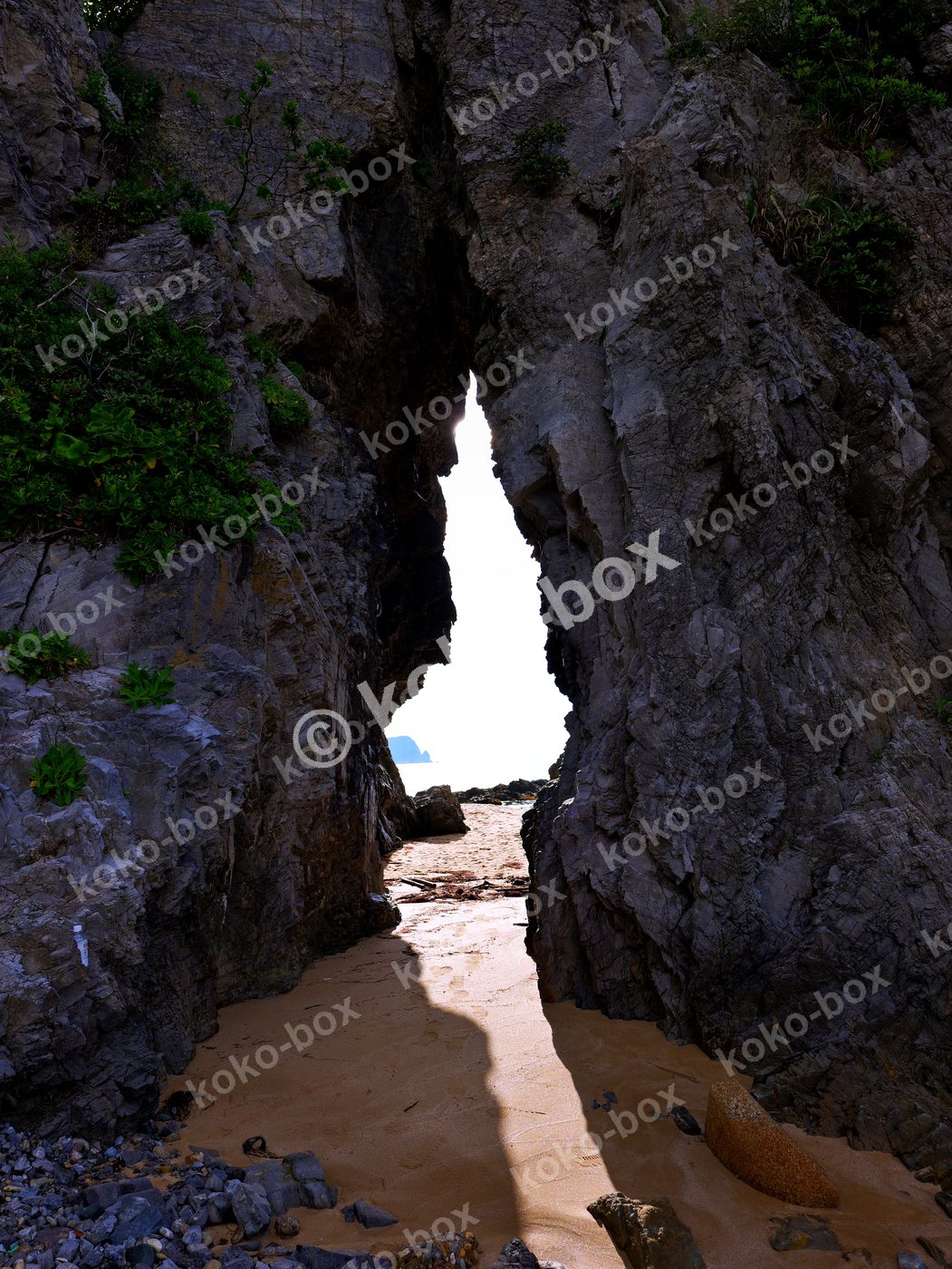 洞窟から望む輝く砂浜と海 縦位置写真素材