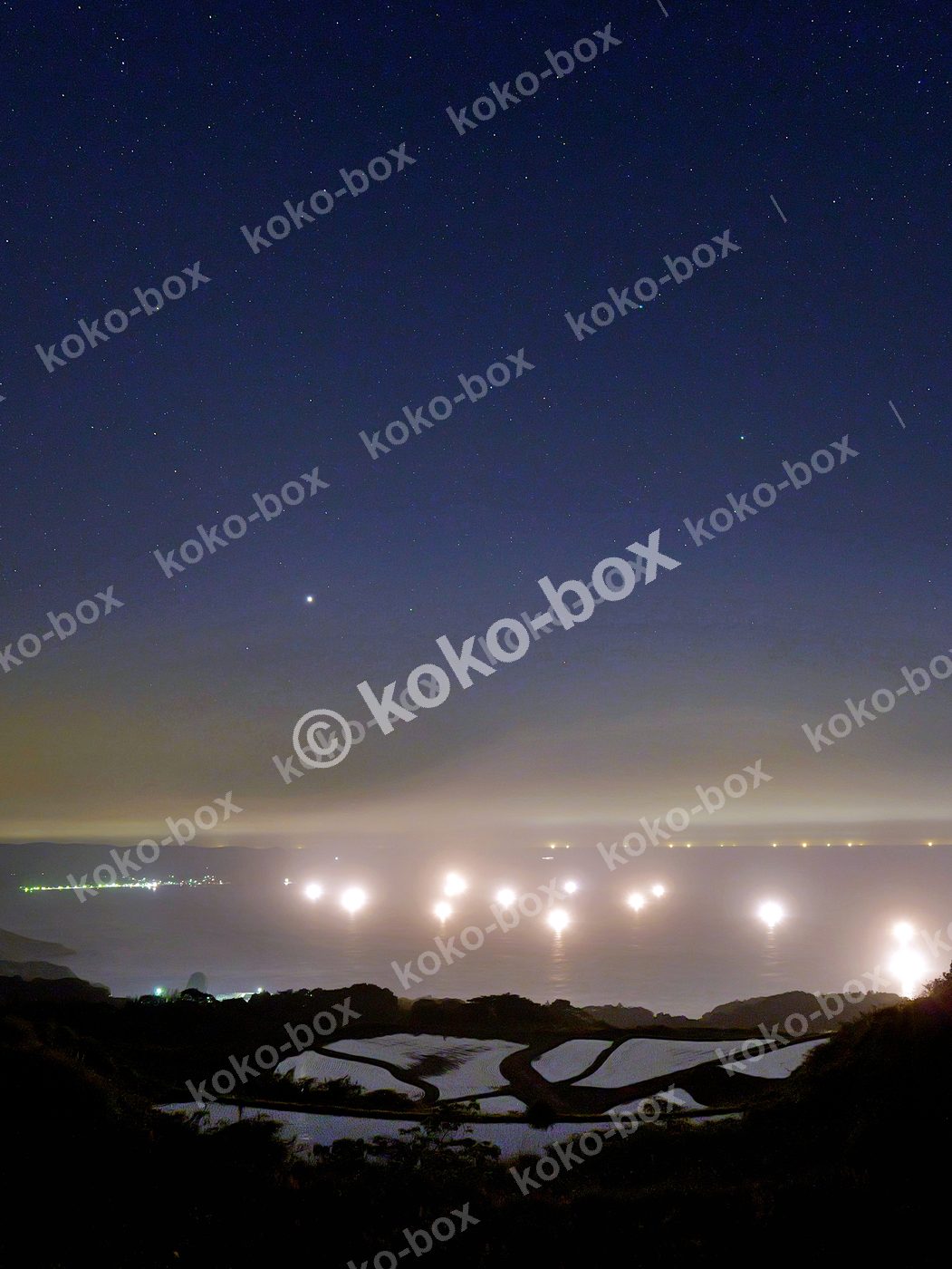 海に浮かぶ漁火と棚田の夜景 縦位置写真素材