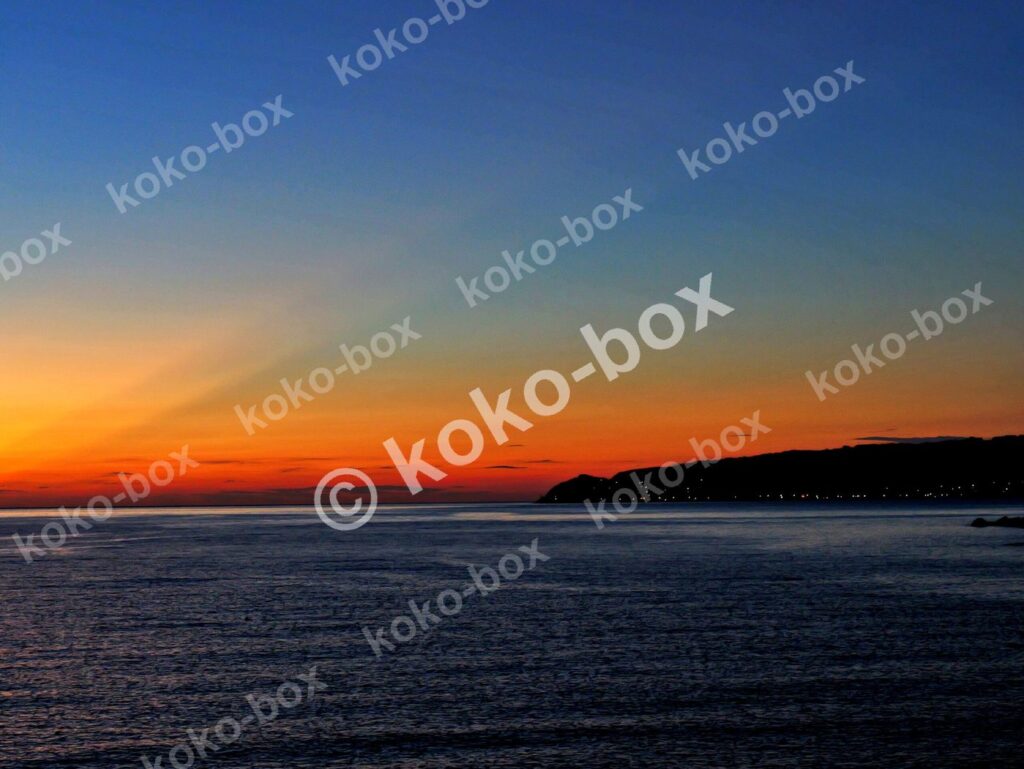 水平線と島、赤オレンジの射線が幻想的な夕焼けグラデーション 写真素材