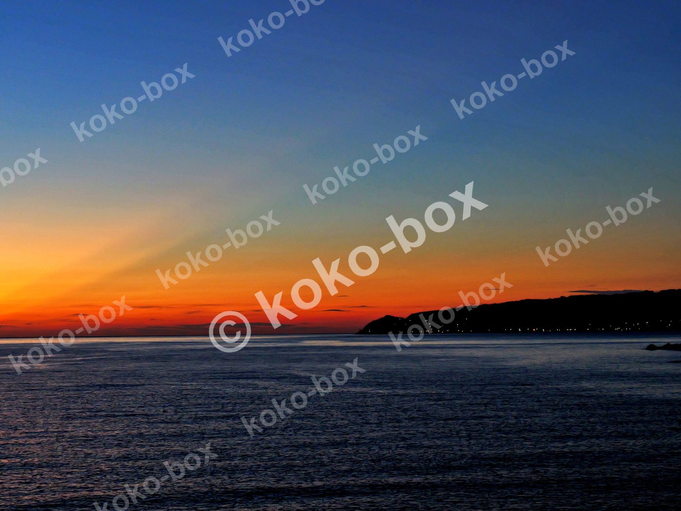 水平線と島、赤オレンジの射線が幻想的な夕焼けグラデーション 写真素材