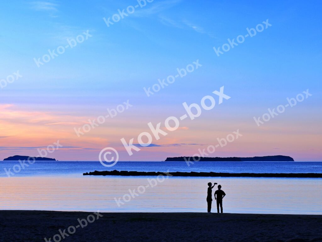 夕暮れの海岸線と二人のシルエット 横位置 写真素材