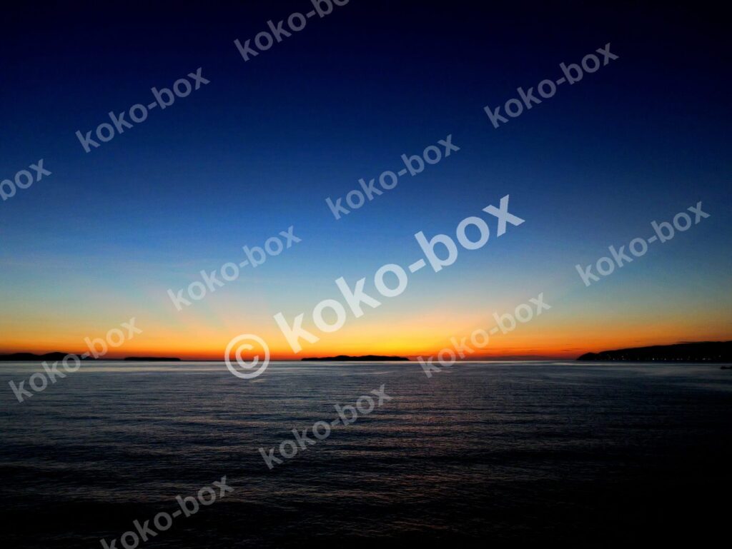 水平線と島、赤オレンジの射線が幻想的な夕焼けグラデーション 写真素材