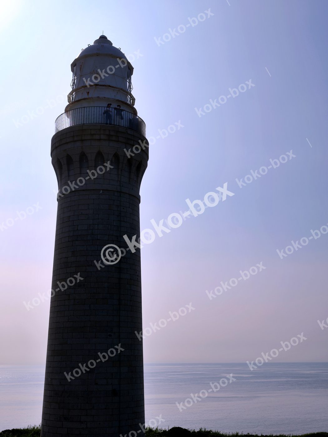 夕暮れの海と石造り灯台の縦位置写真
