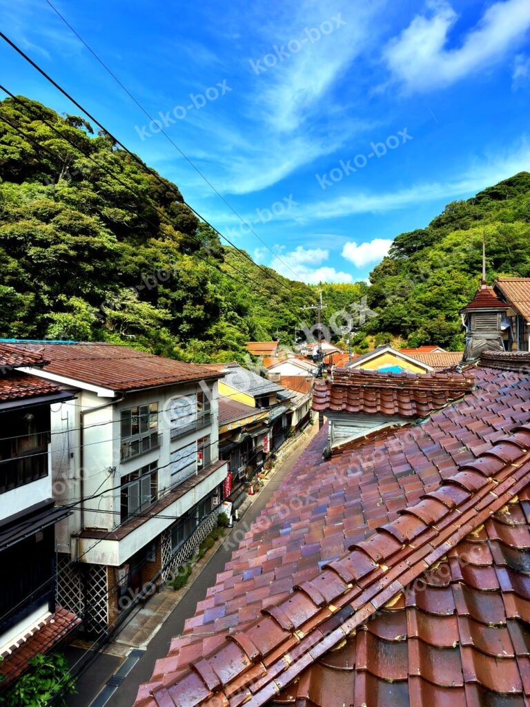 日本のひなびた温泉街、赤瓦の屋根と山々の風景 縦位置