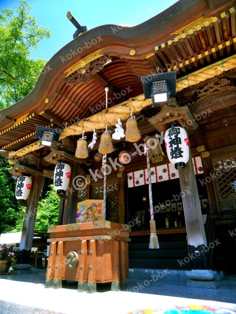 新緑と青空に包まれた神社の拝殿と注連縄の縦位置写真