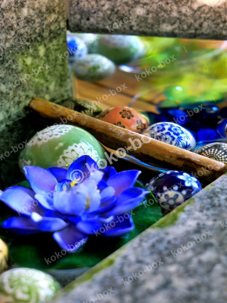 石の器に浮かぶ青い蓮の花と和柄の浮き玉の縦位置写真