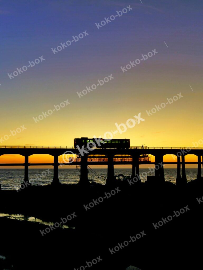 夕焼けの海と高架橋を走る列車のシルエット 縦位置写真