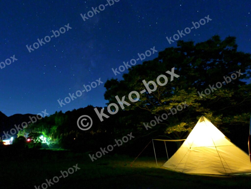 満天の星空と温かく輝くティピー型キャンプテント 横位置