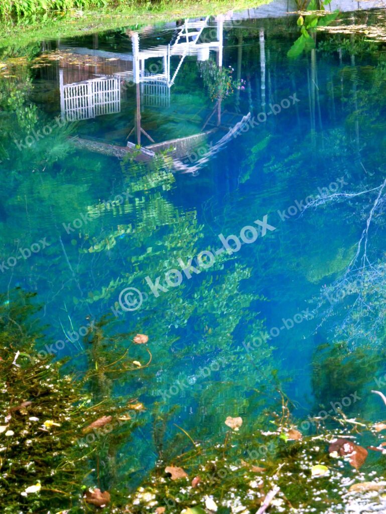 神秘的な蒼の泉と水底に沈むボート 縦位置写真