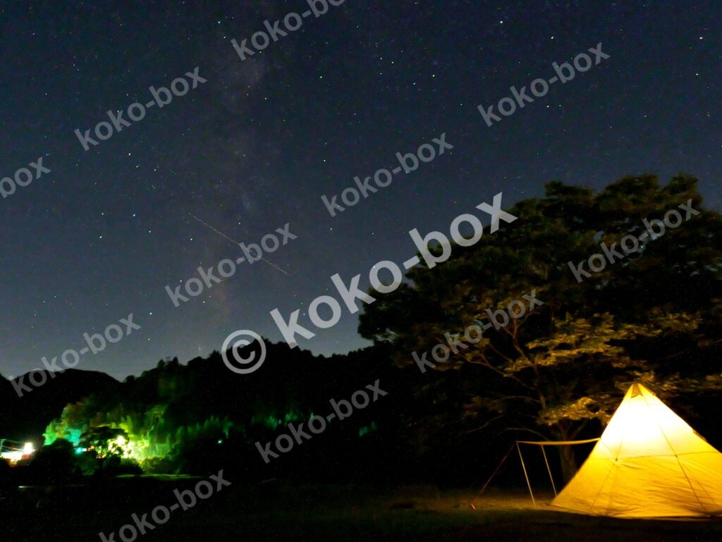 天の川と流れ星の下で光るワンポールテントのキャンプ風景 横位置写真